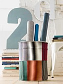 Rolls of paper in striped bin in front of stacked books and decorative number