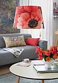 A living room with a sofa, coffee table and a pendant lamp with a poppy shade