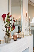 Vase mit Calla-Blüten und Beerenzweigen, Windlichter und Kerzenständer auf Kaimnsims vor Spiegel