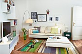 White media cabinet, wall-mounted shelves, cream sofa, ottoman and striped rug