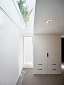 Free standing white cupboard next to a patio door and skylight strips in the ceiling