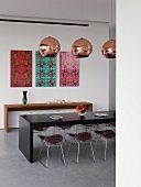 Colourful, graphic artworks behind retro-style dining area with wire chairs, console table and spherical, metallic lamps