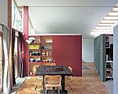 Red room divider with built-in shelves and rustic workbench in front of a bank of windows