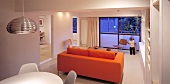 Dining area and orange sofa in a living room in front of a bank of windows