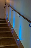 Ascending wood stairway with spot lights recessed in the stringers and illuminated in blue light