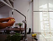 Washing an apple under running water coming out of the kitchen faucet