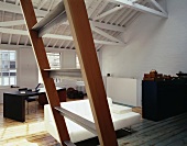 View through a wooden ladder into an open living room of a factory building of a white sofa and writing desk