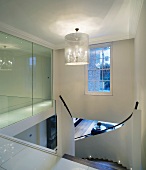 Designer stairwell with pendant lamps and glass partition next to curved staircase