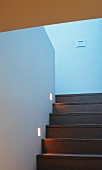 Purist stairwell with recessed spotlights in wall next to treads