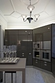 Table with champagne glasses on a tray and kitchen cabinets with built-in appliances in brown, glossy cabinets in a stately home