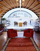 Red armchairs on a platform with dining area in an open room under a barrel roof