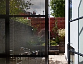 Window with partially closed blinds and view through and open patio door of a city garden