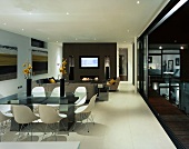 White shell chairs in front of a modern dining table in an open living room with open terrace door with a view of a pool in the evening light