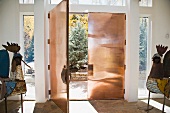 Artistic metal work next to an open entrance door made of copper and view into a garden