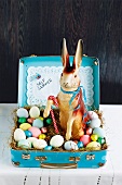 A papier-mâché rabbit with Easter eggs and chocolate eggs in a child suitcase