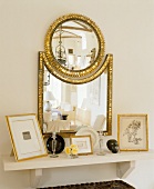 Framed pictures on a white wall shelf with a combination of mirror with golden frames above it