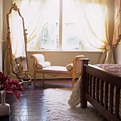 An antique chaise lounge in front of a large floor mirror in a bedroom
