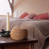 A wicker box and a candle on a small table in a bedroom