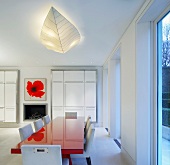 Open-plan dining room with red painted dining table and white upholstered chairs in front of made-to-measure cupboards