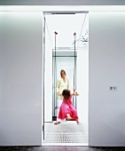 View through doorway to mother pushing daughter on swing in light stairwell