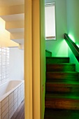 Glowing green lights integrated into handrail of a stairway next to a white-tiled bathroom