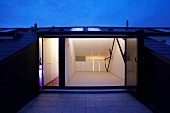 Roof terrace at dusk with view of illuminated, empty interior with white fitted cupboards