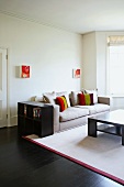 Small paintings above upholstered sofa with scatter cushions and simple black furniture