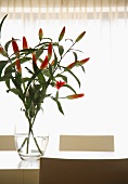 Glass vase with red lilies against the light on a modern dining table