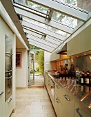 Glass roof above long kitchen counter with spotlights reflected in stainless steel worktop