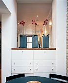 Three red orchids in square pots on fitted chest of drawers in wall opening