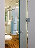 View through open door into modern bathroom with toilet and inlaid wooden floor
