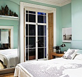 Modern double bed in front of terrace door in traditional light blue bedroom