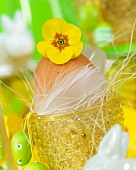 An egg in an egg cup decorated with flowers, feather and Easter eggs