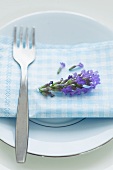 A fork, a napkin and a lavender flower on a plate