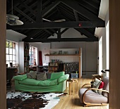 Cow skin on floorboards in front of green upholstered sofa in loft-style living space with dark wood roof beams