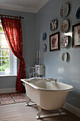 Freestanding bathtub in blue bathroom with red curtains and wall plates