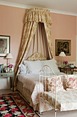 Bedroom with four-poster bed and floral bedspread, pink wallpaper and bedside tables with flower vases