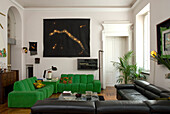 Wohnzimmer mit grüner Eckcouch, schwarzem Ledersofa und Gemälde an der Wand