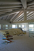 Dachgeschoss-Schlafzimmer mit Holzbalkendecke und Bücherstapeln auf Teppichboden