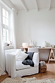 Weisser Atelierwohnraum mit Hussensessel vor hohem Sprossenfenster und Keramikvasen auf einer Tischplatte im Hintergrund