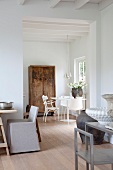 White interior in renovated country house with vessels on three tables of different styles and old wooden cupboard in background