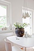 Dark clay pot of flowers on modern table contrasting with country-house interior and various ceramics in snowy white
