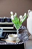 weiße Tulpen im Glas und Kaffeetasse auf Tablett im Zebralook