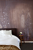 Schlafzimmer mit Wandmalerei, Leoparden-Bettdecke und Holzhocker