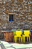Steintisch mit gelben Stühlen vor rustikaler Steinwand im Außenbereich