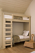 Etagenbett aus hellem Holz im minimalistischen Schlafzimmer mit Korbsessel