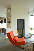 Orange easy chair in front of open fire in modern living-dining room