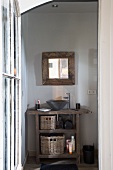 View through open door of mirror and rustic washstand with countertop ceramic basin next to designer tap fitting