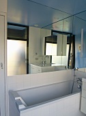Modernes Bad mit Badewanne unter grossflächigem Spiegel an Wand