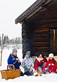 A family grilling sausages on a open fire in front of a mountain hut